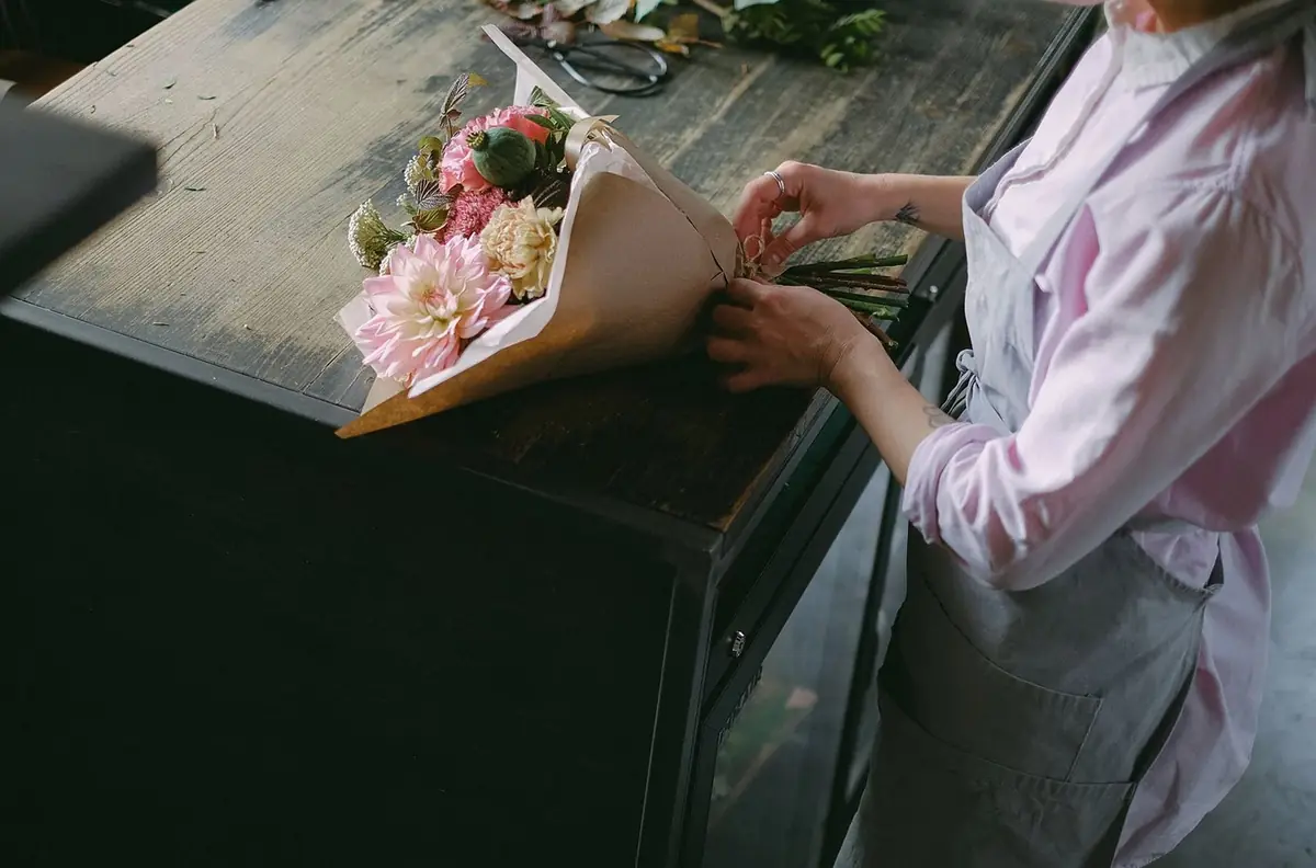 Hands wrapping a large bouquet in kraft paper on a dark table (illustrative photo)